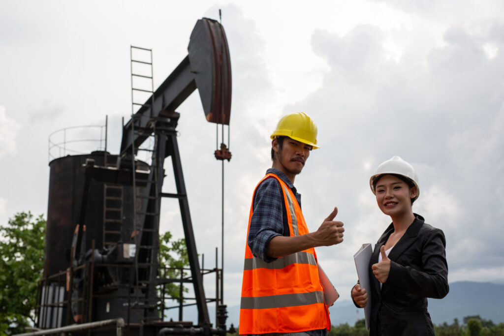 female engineers consult with workers working oil pumps with sky