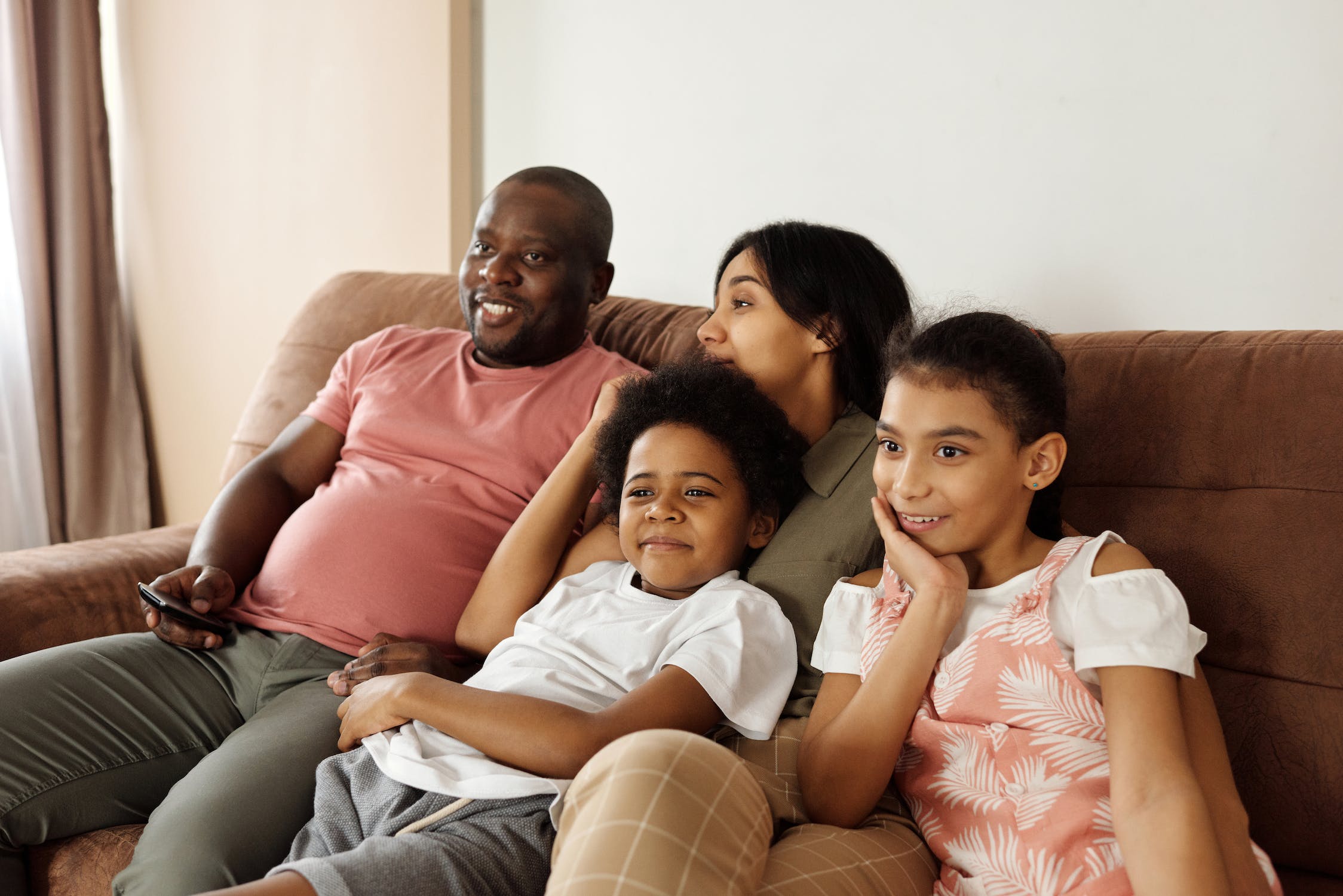 Orang tua dan kedua anaknya sedang duduk di sofa