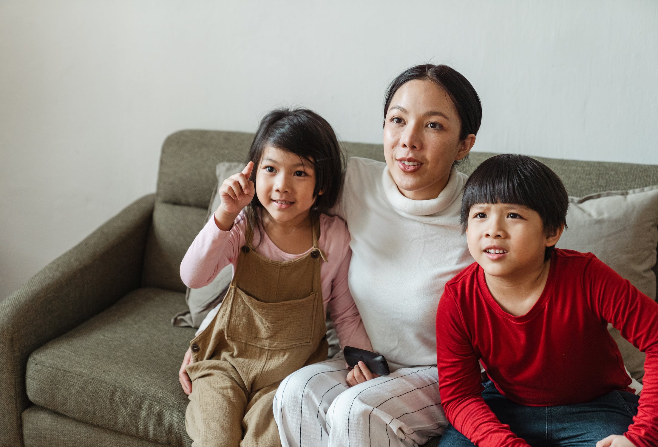 Ibu dan kedua anaknya sedang duduk di sofa 