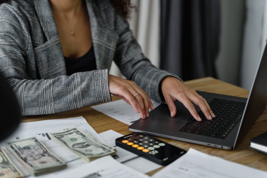 Seorang wanita sedang bekerja dengan laptop, bersama uang dan kalkulator di depannya 